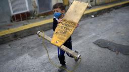 Seorang anak laki-laki membawa carrucha saat mengikuti lomba jalanan tradisional "carruchas", sebutan untuk mobil kayu darurat di Caracas, Venezuela, Sabtu (18/12/2021). Anak laki-laki dan perempuan berusia antara 4 hingga 15 tahun berpartisipasi dalam perlombaan tersebut. (AP Photo/Ariana Cubillos)