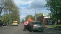 Sebuah mobil tiba-tiba saja mengeluarkan api dari dalam kabin. Sesaat setelah itu, seorang perempuan dari dalam mobil keluar. 