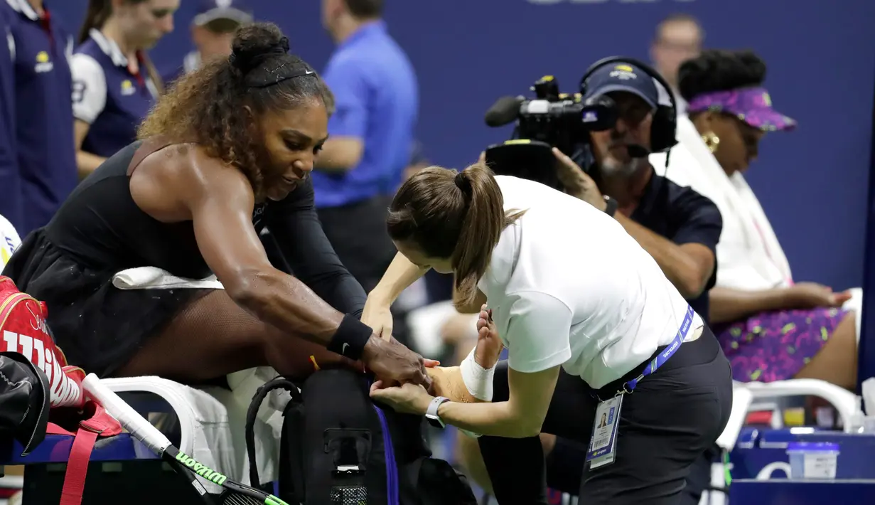 Seorang trainer memeriksa pergelangan kaki Serena Williams saat bertanding menghadapi kakanya, Venus Williams di putaran ketiga turnamen tenis AS Terbuka di New York, Jumat (31/8). Serena mengalahkan Venus dengan skor 6-1, 6-2. (AP Photo/Julio Cortez)