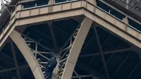 Petugas pemadam kebakaran berusaha mendekati seorang pria yang memanjat Menara Eiffel tanpa peralatan keselamatan di Paris, Senin (20/5/2019). Pasukan pemadam kebakaran harus turun dari lantai tiga dek observasi Menara Eiffel untuk mencapai pria itu. (FRANCOIS GUILLOT / AFP)