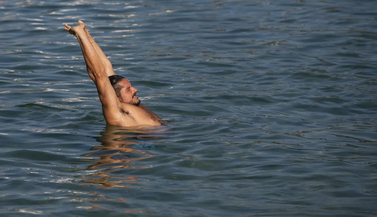 Seorang pria meregangkan tubuh di pantai Arpoador selama gelombang panas di Rio de Janeiro, Brasil, pada hari libur kota Saint Sebastian, Kamis (20/1/2022). (AP Photo/Bruna Prado)