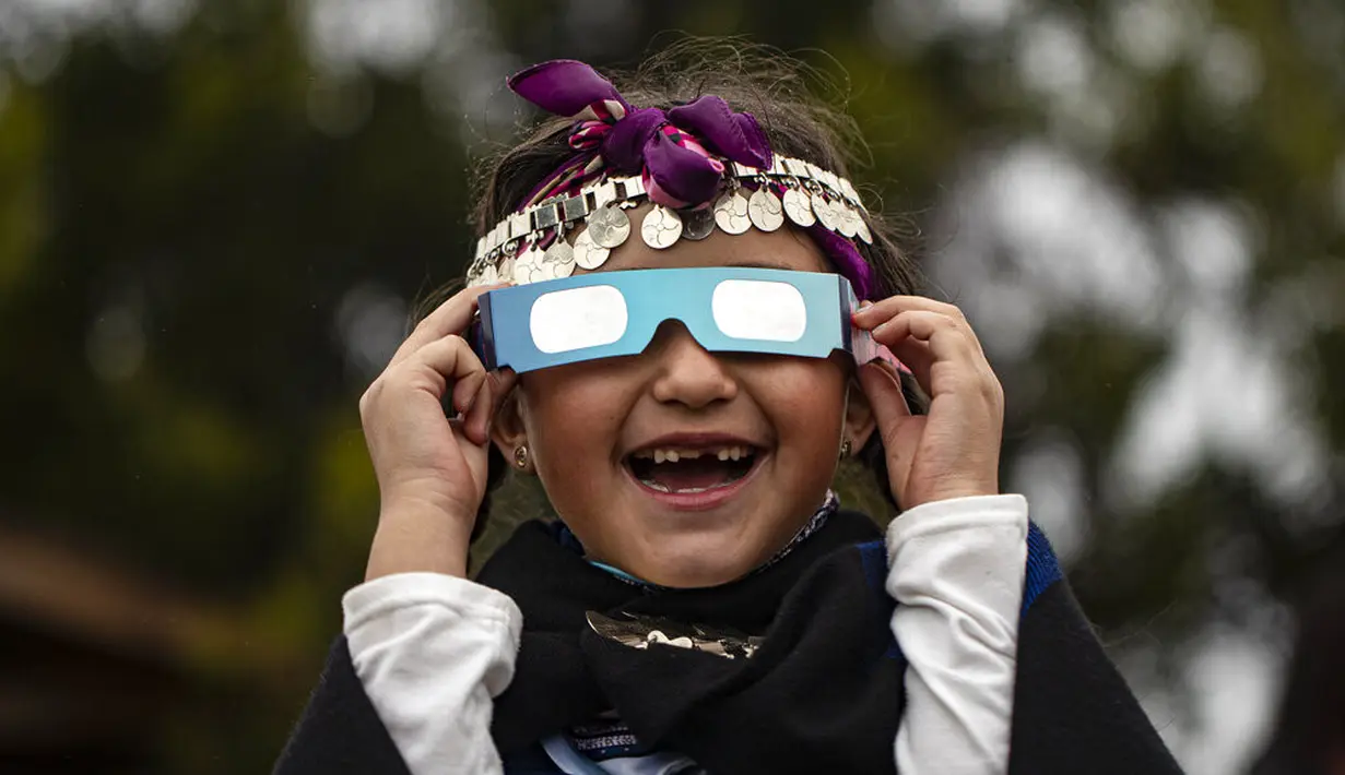Magdalena Nahuelpan, seorang gadis Adat Mapuche, melihat gerhana matahari total menggunakan kacamata khusus di Carahue, La Araucania, Chile, Senin (14/12/2020). Gerhana matahari total terlihat dari Chile dan wilayah Patagonia utara Argentina. (AP Photo/Esteban Felix)