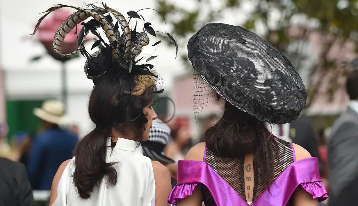 Dua orang wanita berjalan memakai hiasan kepala saat menyaksikan kompetisi balap kuda Melbourne di arena pacuan kuda Flemington Racecourse di Melbourne, Australia (1/11). Balap kuda ini diselenggarakan pertama kalinya pada tahun 1861. (AFP/Paul Crock)