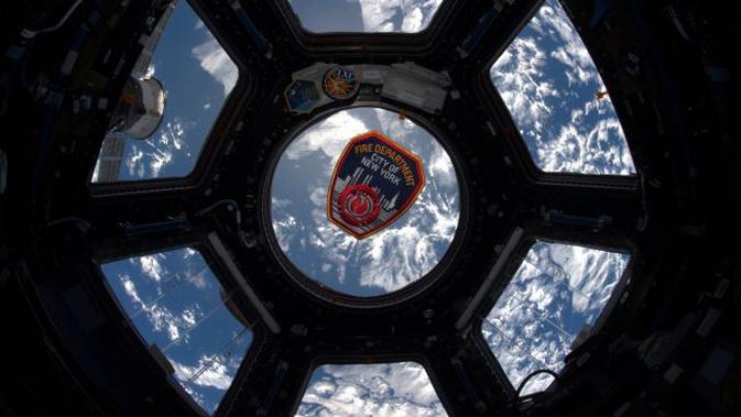 Sebuah emblem Departemen Pemadam Kebakaran Kota New York mengapung di jendela Cupola dari Stasiun Luar Angkasa Internasional pada peringatan 18 tahun serangan teror 11 September (9/11). ( NASA)