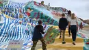 Turis mengunjungi Salvation Mountain, sebuah lereng bukti di Niland, California, Amerika Serikat. Salvation Mountain memiliki lebar 46 meter, dan panjang 15,2 meter ini tidak dihiasi pepohonan, melainkan tulisan dan gambar warna-warni dengan pesan cinta. (Robyn Beck/AFP)