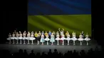 Penari Ukraina dari Balet Kota Kiev menerima tepuk tangan di depan bendera Ukraina yang diproyeksikan ke layar di akhir pertunjukan, di Theater de Chatelet, Paris (8/3/2022). Balet Kota Kiev menari dengan penuh semangat di Paris untuk pertunjukan terakhir dari tur Prancis. (AP Photo/Thibault Camus)