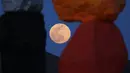 Supermoon terlihat dari celah instalasi seni Seven Magic Mountains karya seniman Ugo Rondinone di Las Vegas, Amerika Serikat, Selasa (7/4/2020). Warna-warni tumpukan batuan besar di tengah Gurun Nevada menjadikan Seven Magic Mountains terlihat sangat Instagramable. (AP Photo/John Locher)
