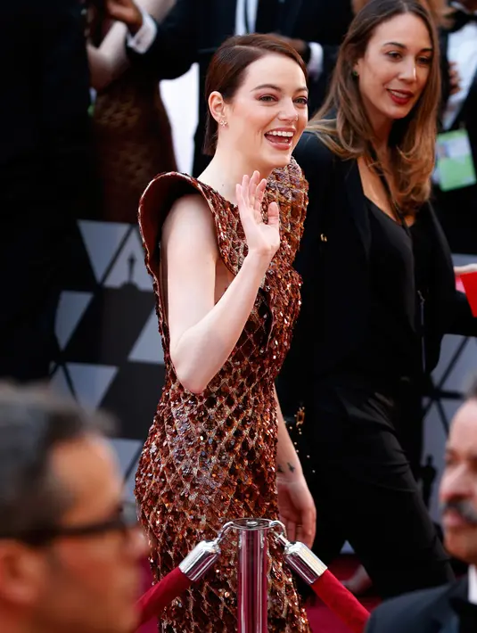 Aktris Emma Stone menyapa fans saat tiba menghadiri perhelatan Piala Oscar 2019 di Teater Dolby di Los Angeles, AS (24/2). Emma Stone tampil cantik mengenakan gaun emas seperti sarang lebah Louis Vuitton. (AFP Photo/Eric Jamison)