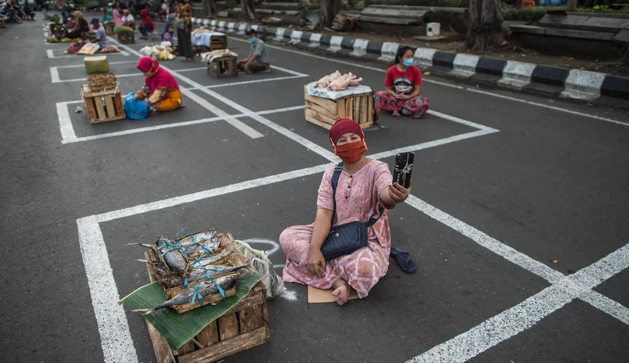 Pedagang menunggu pembeli di dalam garis petak-petak untuk menerapkan jaga jarak (physical distancing) di sepanjang jalan di Surabaya, Selasa (2/6/2020). Garis petak-petak bagi pedagang itu sebagai langkah pencegahan penyebaran COVID-19. (Photo by Juni Kriswanto / AFP)