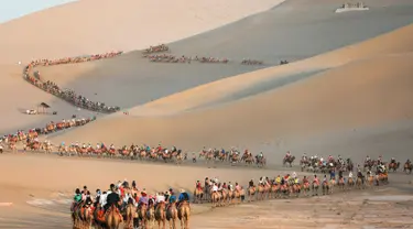 Para wisatawan menaiki unta di padang pasir di Dunhuang di provinsi Gansu di China barat laut (10/8/2019). Dunhuang adalah sebuah kota tingkat kabupaten di barat laut provinsi Gansu, Tiongkok Barat. (AFP Photo/Str)