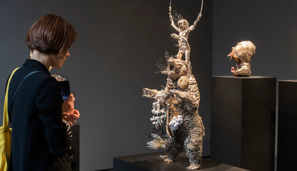 Seorang wanita melihat patung yang berjudul "Demon with Bowl" karya seniman Inggris, Damien Hirst saat pameran di Venice, Italia (6/4). Karya itu sebelumnya direndam dalam laut hingga teroksidasi dan menimbulkan lapisan karang. (AFP Photo/Miguel Medina)