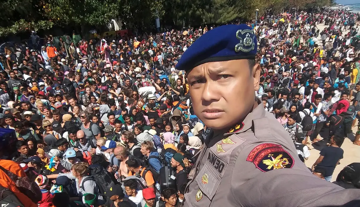 Kepala Polair Lombok, Dewa Wijaya berswafoto dengan latar ratusan orang yang berusaha meninggalkan Gili Trawangan, NTB, Senin (6/8). Lebih dari seribu turis dievakuasi dari pulau-pulau kecil di Gili Trawangan. (Handout/Indonesia Water Police/AFP)