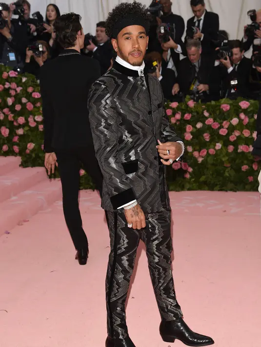 Pembalap Mercedes, Lewis Hamilton berpose saat tiba menghadiri Met Gala 2019 di Metropolitan Museum of Art di New York, AS (6/5/2019). Lewis Hamilton menjadi pusat perhatian dengan setelan jas hitam berdesain zig-zag metalik dan ikat kepala bertatahkan permata.  (AP Photo/Evan Agostini)