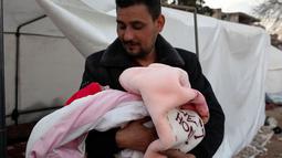 Khalil al-Suwadi menggendong keponakannya Afraa, bayi Suriah yang lahir di bawah reruntuhan setelah gempa bumi 6 Februari yang melanda Turki dan Suriah yang menewaskan orang tua dan saudara kandungnya, di kota Jindayris yang dikuasai pemberontak di Suriah utara, Selasa (21/2/2023). Afraa adalah salah satu dari sekian banyak anak yatim piatu akibat gempa dahsyat tersebut. (Rami al SAYED / AFP)