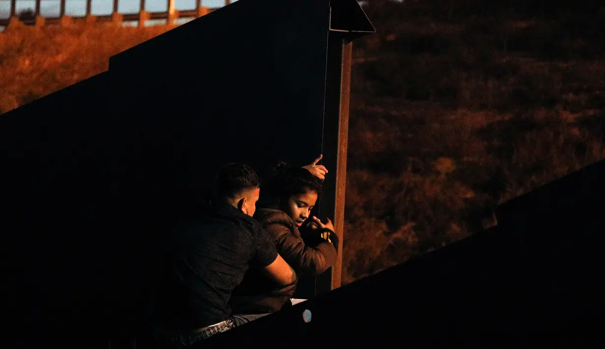 Seorang pria membantu seorang wanita memanjat pagar erbatasan AS dari Playas de Tijuana, Meksiko (3/12). Ribuan imigran dari Amerika Tengah melakukan perjalanan menuju Amerika Serikat dalam rombongan atau karavan. (AP Photo/Rebecca Blackwell)