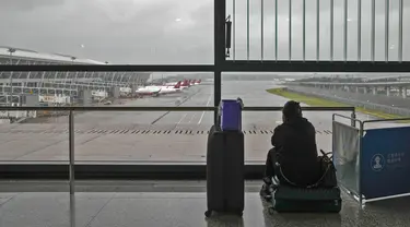 Seorang calon penumpang duduk di kopernya mengamati pesawat yang diparkir di landasan setelah semua penerbangan dibatalkan di Bandara Internasional Pudong, Shanghai, Minggu (25/7/2021). Ratusan jadwal penerbangan dibatalkan saat topan In-Fa bergerak menuju mendarat. (AP Photo/Andy Wong)
