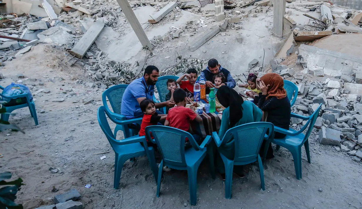 Sebuah keluarga Palestina berbuka puasa di sebelah rumah mereka yang hancur selama eskalasi dua hari, di Rafah, Jalur Gaza selatan (8/5/2019). Perang yang terjadi antara Gaza dan Israel masih berlangsung hingga detik ini. (AFP Photo/Said Khatib)