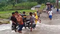 Sejumlah pemuda sedang mengangkat motor milik warga untuk menyebrangi sungai akibat banjir bandang. (Liputan6.com/ Dionisius Wilibardus)
