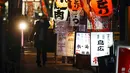 Seorang wanita yang mengenakan masker untuk mengekang penyebaran virus corona COVID-19 berjalan melewati sebuah bar di Tokyo, Jepang, Rabu (6/1/2021). Ibu kota Jepang itu mengkonfirmasi lebih dari 1.500 kasus baru virus corona COVID-19 pada 6 Januari 2021. (AP Photo/Eugene Hoshiko)