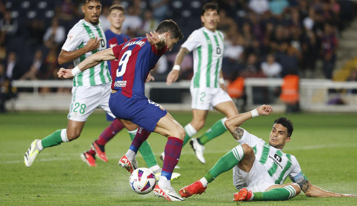 Pemain Barcelona, Robert Lewandowski, berusaha melewati pemain Real Betis pada laga Liga Spanyol di Estadi Olimpic Lluis Companys, Minggu (17/9/2023). Barca menang dengan skor 5-0. (AP Photo/Joan Monfort)