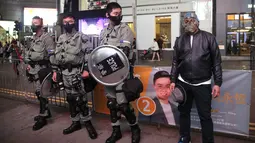 Seorang pria bertopeng Halloween berdiri di sebelah petugas polisi yang mengenakan pakaian anti huru hara di Hong Kong, Kamis (31/10/2019). Peraturan larangan penutup wajah dibuat untuk membantu memadamkan protes yang semakin memanas di bulan kelima. (AP Photo/Kin Cheung)